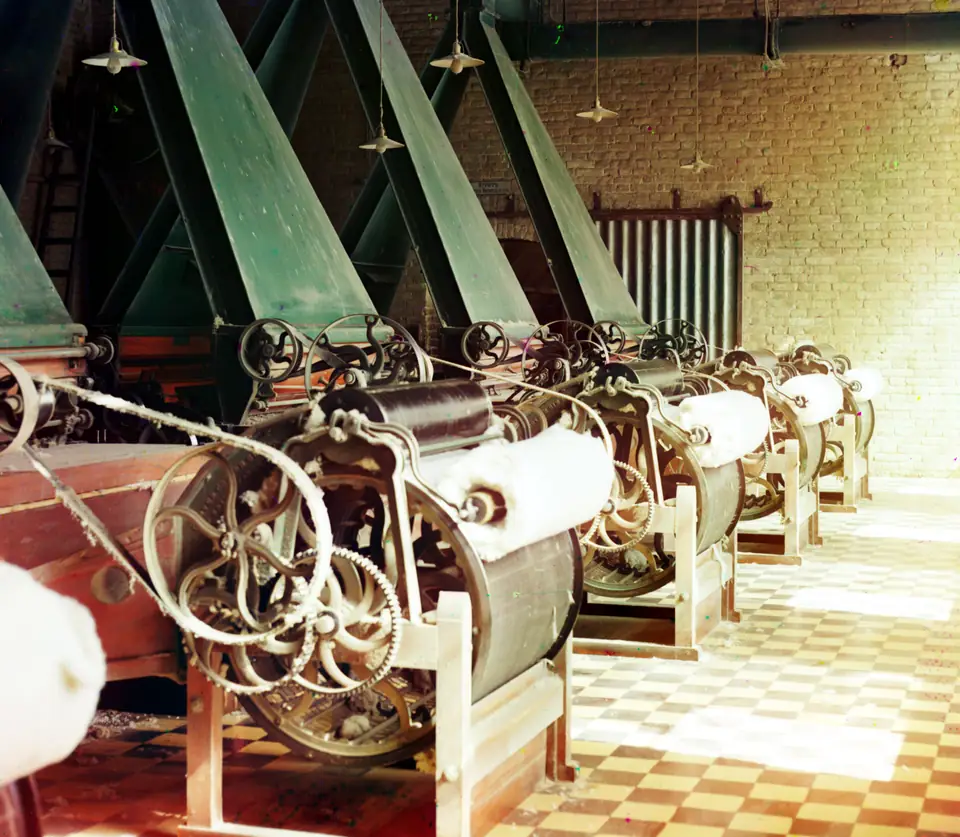 Rows of spinning machines inside a cotton mill, with workers between them