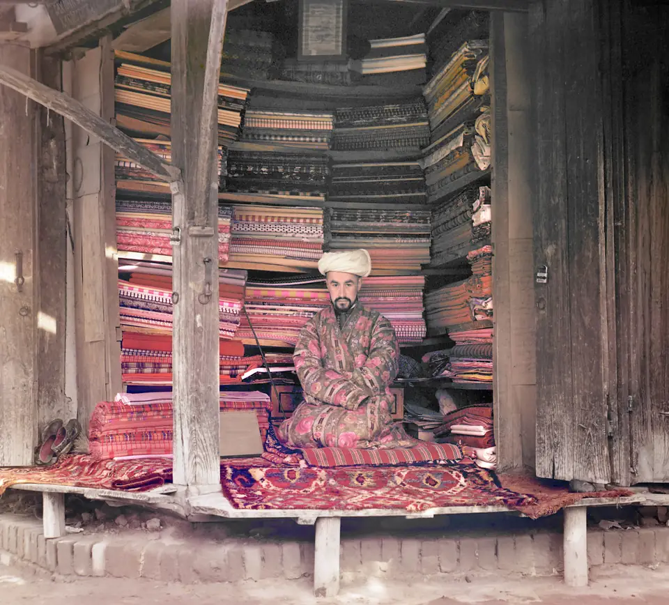 A merchant seated in his shop with bolts of silk, cotton and wool on display
