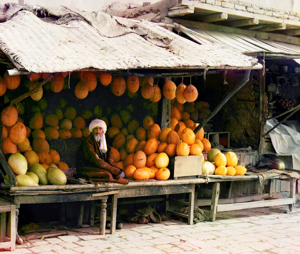 A melon seller sitting among stacks of melons at a market stall in Samarkand